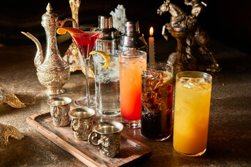 A tray of drinks with a mix of cocktails and juices. The drinks are served in various glasses and cups, including martini glasses, shot glasses, and tall glasses