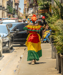 Photograph of a Colombian woman in Cartagena de Indias walking in the Palenqueras dress. Trip to Colombia. Typical colonial colors of the city.