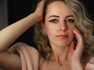 Obraz premium A close-up portrait of a stylish woman with wavy blonde hair, elegant silver rings, and soft makeup, gazing confidently at the camera against a dark background