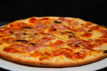 Pizza with ham and mushrooms on a white plate. Black background.