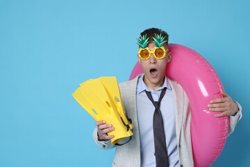 Businessman with inflatable ring, funny sunglasses and flippers on light blue background, space for text