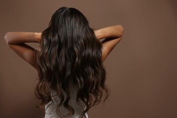 Hair styling. Woman with wavy long hair on brown background, back view