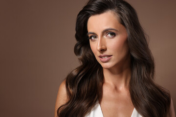 Naklejka premium Hair styling. Portrait of beautiful woman with wavy long hair on brown background, space for text