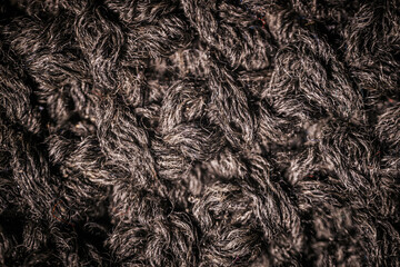 A detailed macro view of dark knitted fabric, showcasing the rich texture and thick yarn weave. The image emphasizes the material's soft and cozy appearance.