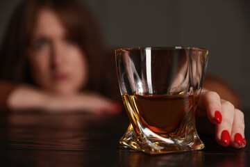 Alcohol addiction. Woman with glass of whiskey at wooden table indoors, selective focus