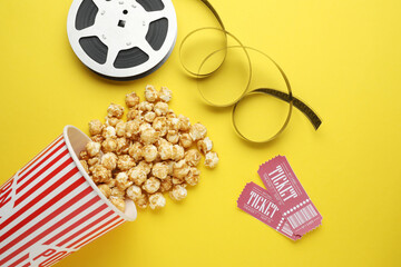 Movie tickets, sweet popcorn and film reel on yellow background, flat lay