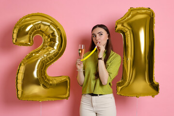 Coming of age party - 21st birthday. Happy young woman with number shaped balloons, glass of...