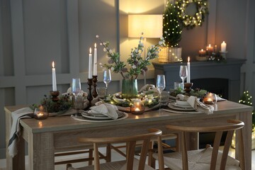 Christmas table setting with stylish dishware, glasses and burning candles in festive decorated room