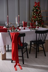 Christmas table setting with stylish dishware, glasses and burning candles in festive decorated room