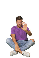 Casual man sitting on floor standing with outstretched hand showing stop sign, preventing you.