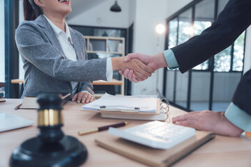 Successful Legal Partnership: Two legal professionals shake hands across a desk, signifying a successful negotiation, agreement, or partnership.  A judge's gavel rests prominently in the foreground.