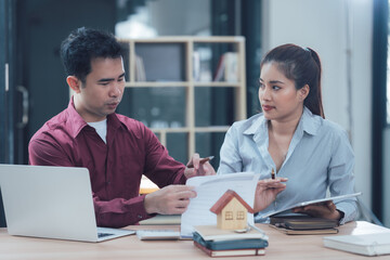 Real Estate Professionals: A  real estate agent and a client discuss paperwork and a model house, a professional and attentive conversation in an office setting.