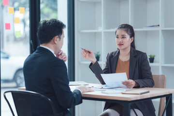 Business Meeting Discussion: Two business professionals, a man and a woman, are engaged in a serious discussion across a table, reviewing documents and exchanging ideas in a modern office setting.  
