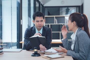 Legal Consultation: A male and female lawyer are engaged in a serious discussion, reviewing documents and using a gavel in a modern office setting.