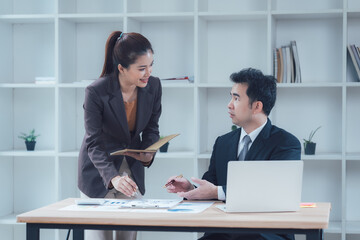 Business Collaboration: A professional business woman in a blazer explains details of a project to her colleague in a modern office setting.