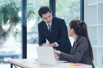 Business Colleagues Collaboration: A focused business meeting unfolds as a male and female colleague collaborate intently over a laptop.