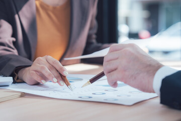 Business Partners Reviewing Documents: Close-up shot of two business partners, a man and a woman, attentively reviewing financial documents, deeply engaged in a collaborative discussion. 