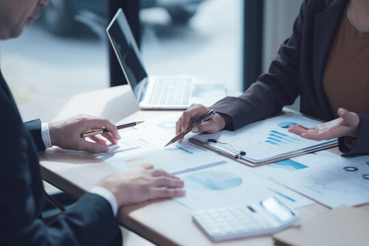Analyzing the Numbers: A close-up shot of two professionals collaborating over a table scattered with charts, graphs, and a calculator.