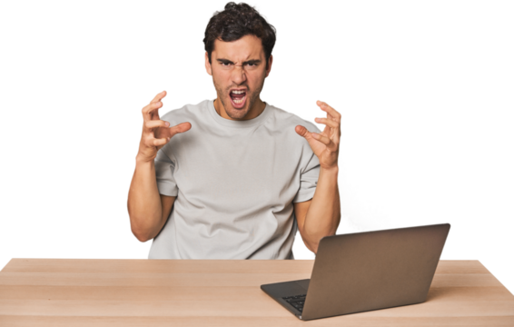 Hispanic young man working on laptop screaming with rage.