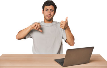 Hispanic young man working on laptop showing thumbs up and thumbs down, difficult choose concept
