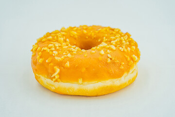 A single, fresh-looking, yellow-glazed doughnut with seed or nut specks sits on a light surface against a neutral backdrop