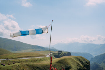 A wind cone with white and blue stripes on the background of a mountain landscape. An outbuilding...