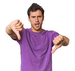 Young Hispanic man in studio showing thumb down and expressing dislike.