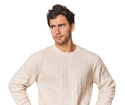 Young Hispanic man in studio confused, feels doubtful and unsure.