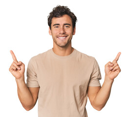 Young Hispanic man in studio indicates with both fore fingers up showing a blank space.
