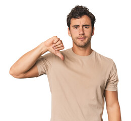 Young Hispanic man in studio showing a dislike gesture, thumbs down. Disagreement concept.