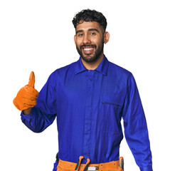 Hispanic worker in blue overalls in studio smiling and raising thumb up