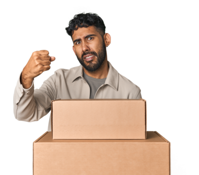 Hispanic male holding cardboard boxes in studio showing fist to camera, aggressive facial expression. - Powered by Adobe