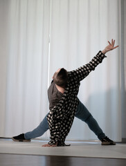 Young guy in a dancing pose on a white background. Modern dance in a plaid shirt. Sports plastic movements of arms and legs and body.