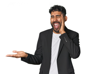 Hispanic businessman in suit in studio holds copy space on a palm, keep hand over cheek. Amazed and delighted.