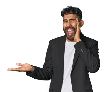 Hispanic businessman in suit in studio holds copy space on a palm, keep hand over cheek. Amazed and delighted.