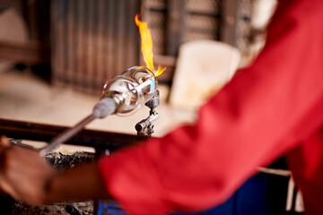 Fire, glassblowing and hands of artisan person closeup in forge for industry, manufacturing or production. Flame, heat and shape with professional industrial craftsman in factory, plant or workshop