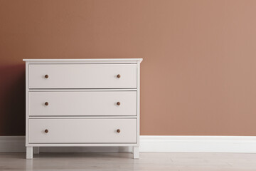 Wooden chest of drawers near wall in shade of mocha mousse. Stylish interior with trendy color of 2025 year
