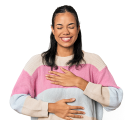 Young Filipina woman laughs happily and has fun keeping hands on stomach.