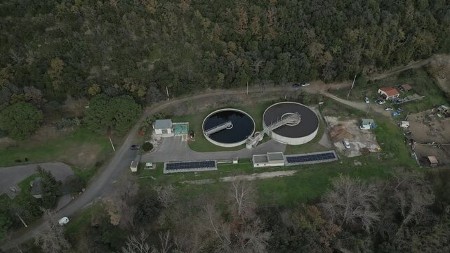 Circular wastewater clarifiers surrounded by solar panels amid forested landscape near amelie les bains palalda. Exemplifying sustainable water management infrastructure in rural french countryside