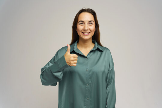 Woman smiles and gives a thumbs up while wearing a light green blouse in a neutral background setting