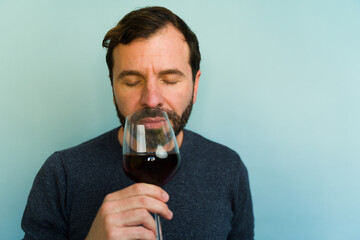 Caucasian man smelling red wine bouquet with closed eyes on blue background