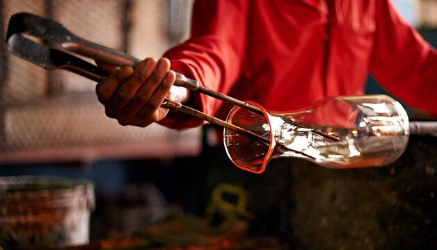 Hands, person and tools in glass factory for shape, production process and industry. Glassware, craft and worker with equipment for manufacturing art, glassblowing and forming with jacks in workshop