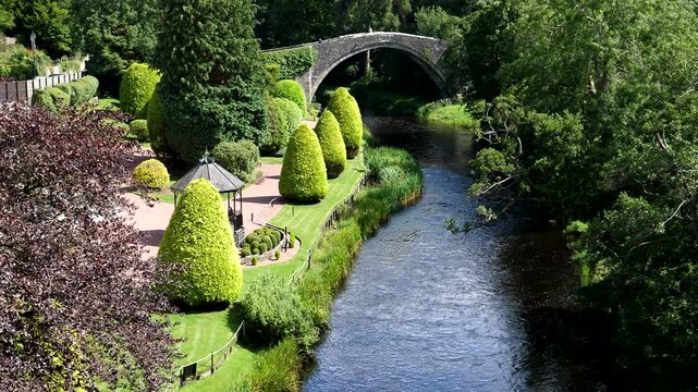 Old stone arch bridge over river Doon in Ayr, Scotland, high angle view of landscaped garden on the riverbank in famous Scottish town in southwest.