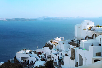 Picturesque view of the Santorini volcano caldera with traditional white houses on the mountainside in Oia against the backdrop of the blue sea.