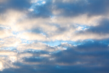 Serene sky filled with a blend of soft, fluffy clouds in varying shades of gray and white. Light blue peeks through the spaces between the clouds, creating a tranquil atmosphere