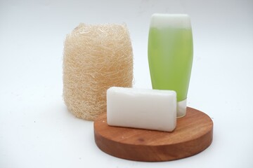 Natural loofah, white soap bar, and green liquid soap on a wooden base, showcasing eco-friendly bath essentials.