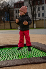 Obraz premium Little cute girl having nice activity time with winter pants in playground at the green in ground trampoline