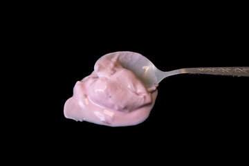 Spoon full of pink strawberry yogurt isolated on black background