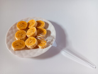 Sweet ripe banana slices with plastic fork on plate isolated on white background.