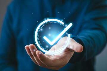 A person holds a glowing check mark floating above their hand, symbolizing approval and success in...